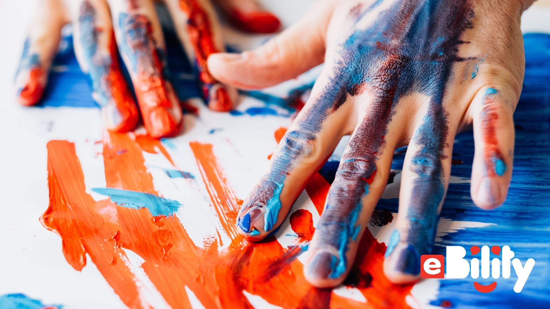 hands and paper covered in blue and orange paint. eBility
